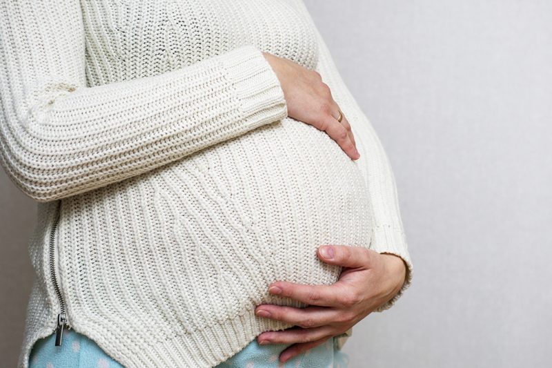 A pregnant woman holds her hands on her belly.