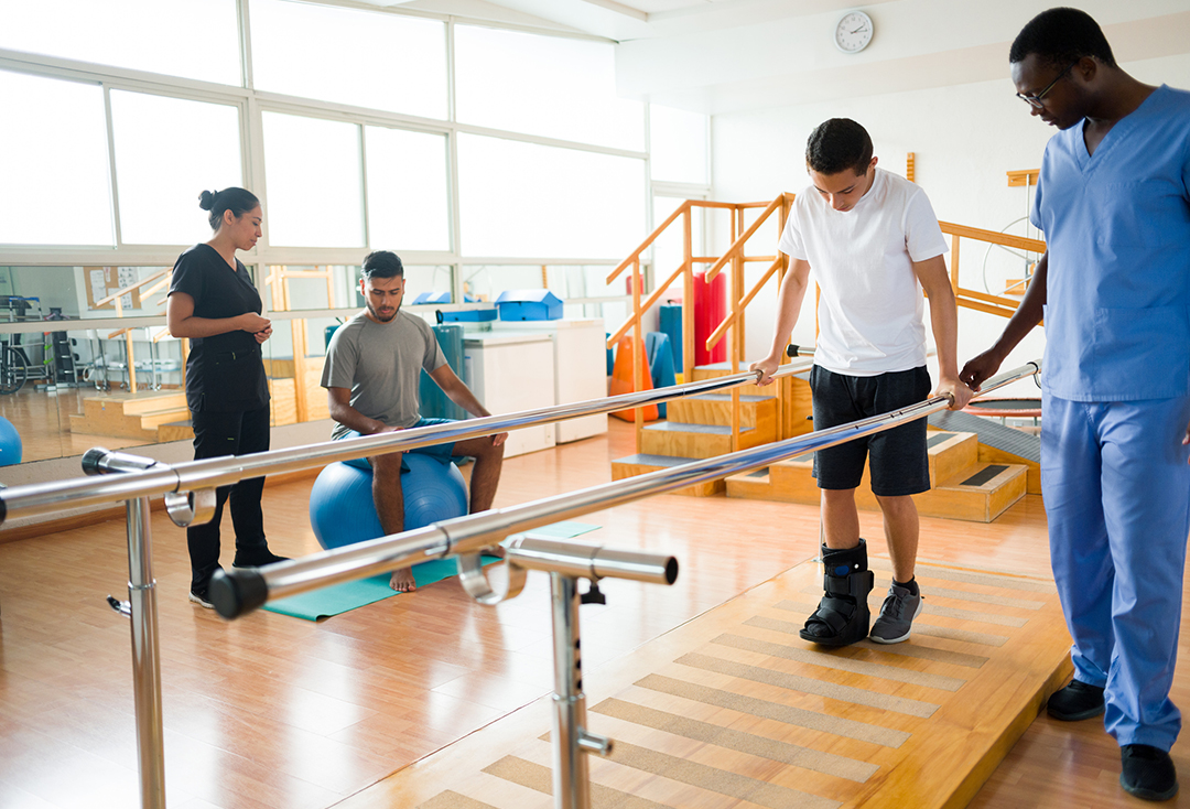 Young men exercising in the physical therapy room next to their health care providers.