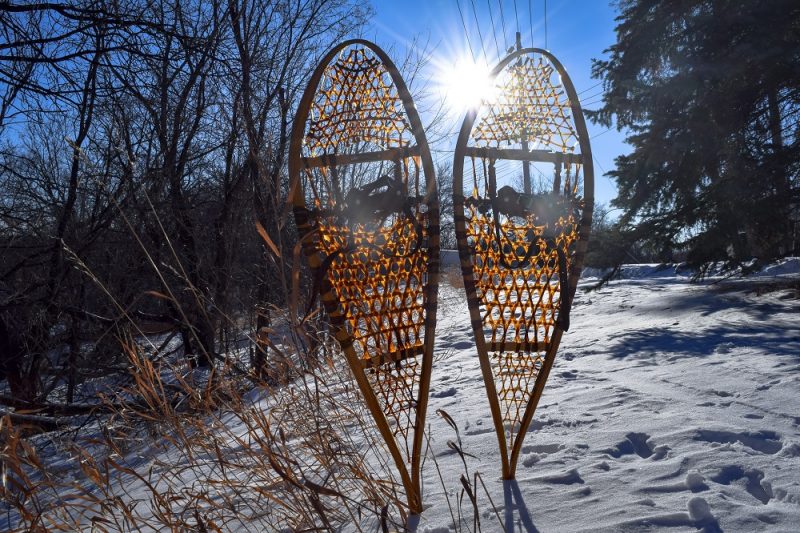 Traditional snowshoes sit in the foreground of a blue sky on a winter day.