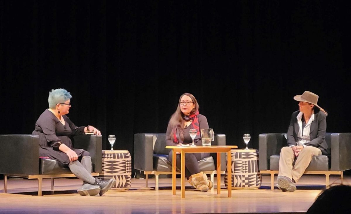 Three women sitting on armchairs on a stage.