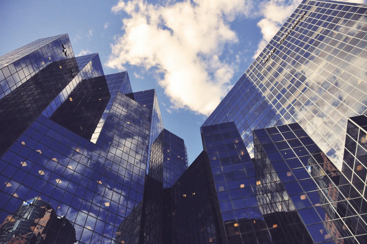 Looking up at tall office buildings in a downtown scene with clouds in a blue sky.