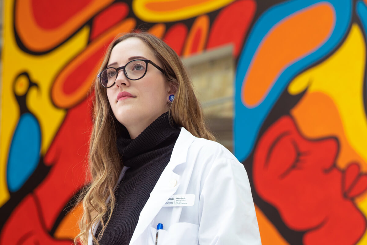 Maizy North looks away in front of Indigenous mural.