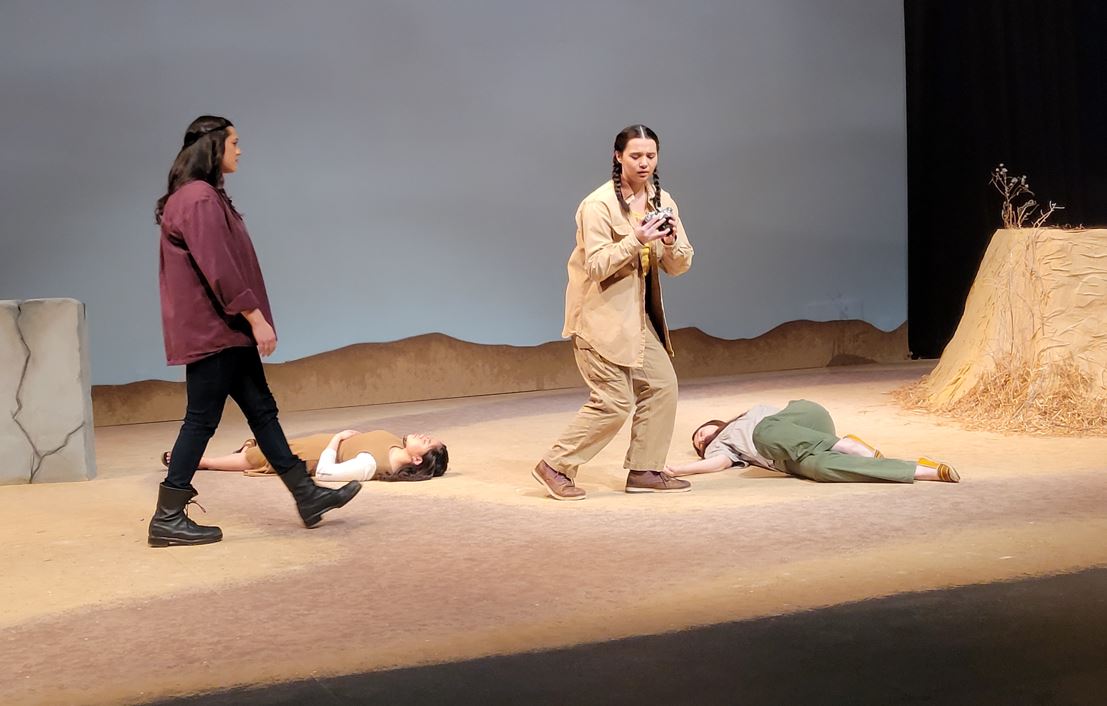 Four student actors on a barren stage. Two actors lying down, one standing and one crouching.