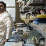 Dr. Vidyanand Anaparti leans against a counter in a lab. He is wearing a white lab coat.