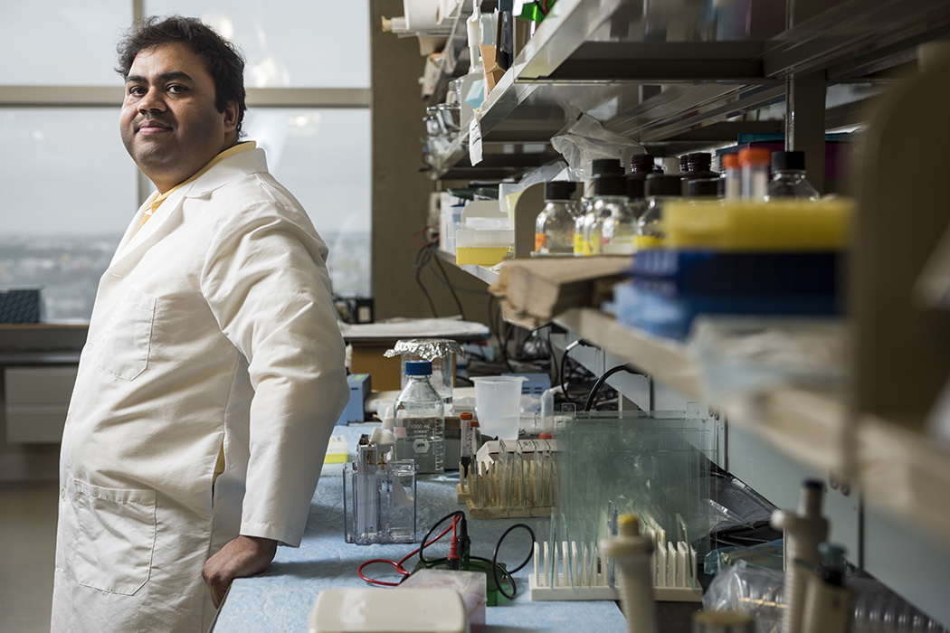 Dr. Vidyanand Anaparti leans against a counter in a lab. He is wearing a white lab coat.