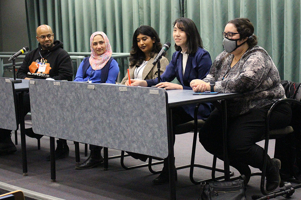 The physicians and students sit at a table. Two microphones sit on the table.