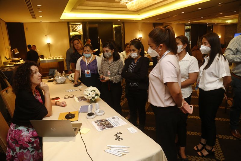 Kim Workum at a conference table speaking to a group of masked nurses.