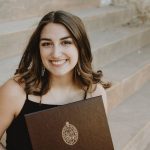 Woman smiling holding her diploma on staircase.