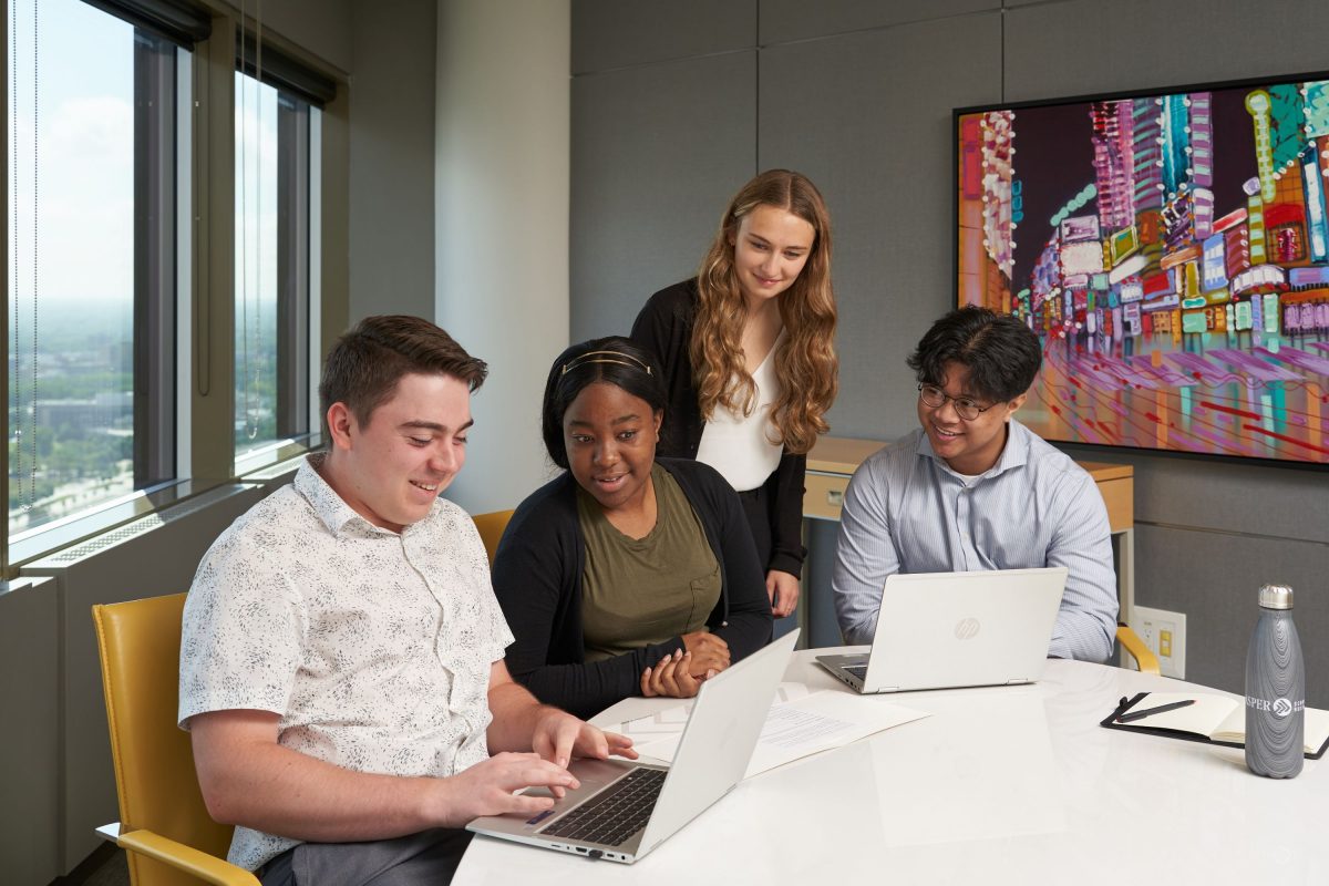 Four students looking at two computers with a big window in the background.