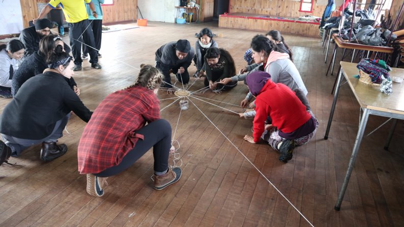 Students holding a web-like string on wood floor.