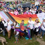 group of people holding a giant progressive pride flag and smiling at the camera