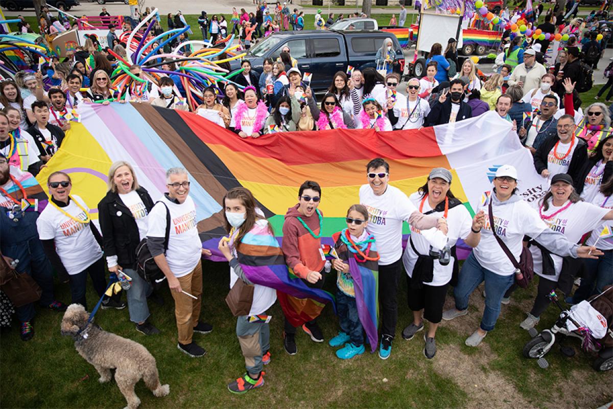 group of people holding a giant progressive pride flag and smiling at the camera