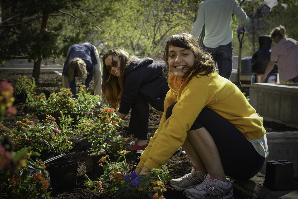 A woman in a yellow hoodie smiles at the camera and planting flowers.