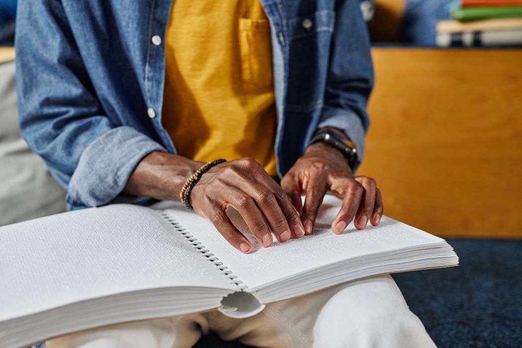 Closeup of a university student with a visual impairment reading a braille book.