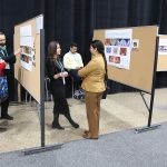 Small groups of people look at research posters at a Research Day event.