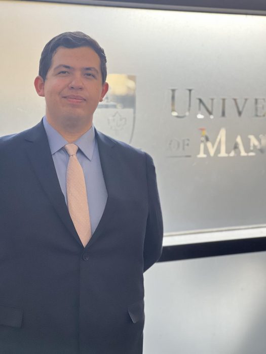 Photo of student in a suit and tie by UM logo.