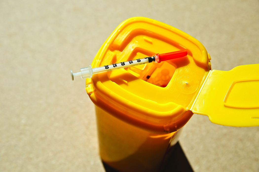 A syringe sits atop a medical waste container inside a hospital.