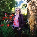 Jen Gunter stands in an outdoor garden between flowers and a brick wall.
