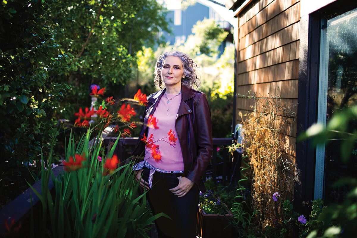 Jen Gunter stands in an outdoor garden between flowers and a brick wall.