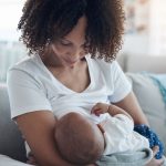 A woman sits on a couch breastfeeding a baby.