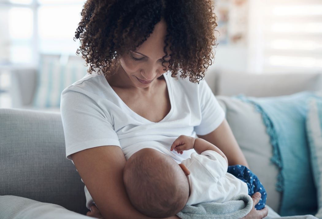 A woman sits on a couch breastfeeding a baby.