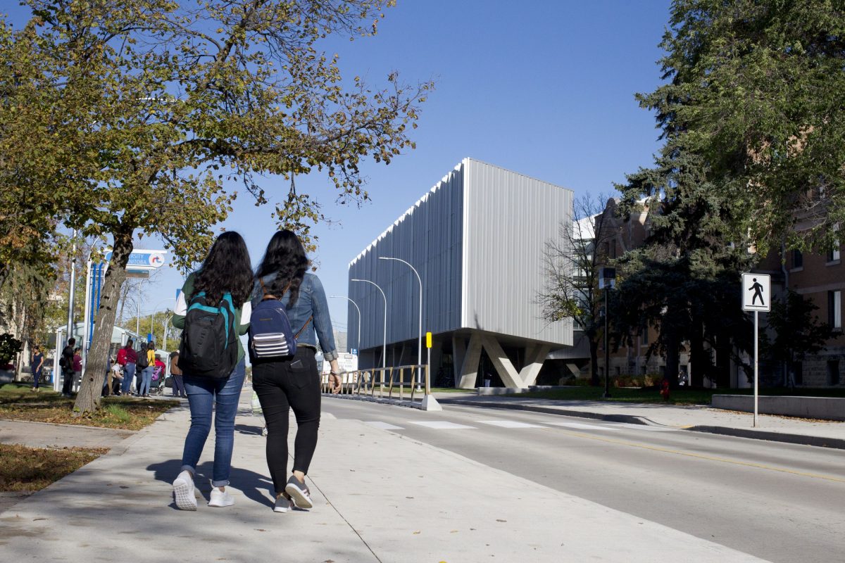 Two students with their backs to the camera walk towards the ArtLab building on the UM's Fort Garry campus