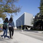 Two students with their backs to the camera walk towards the ArtLab building on the UM's Fort Garry campus