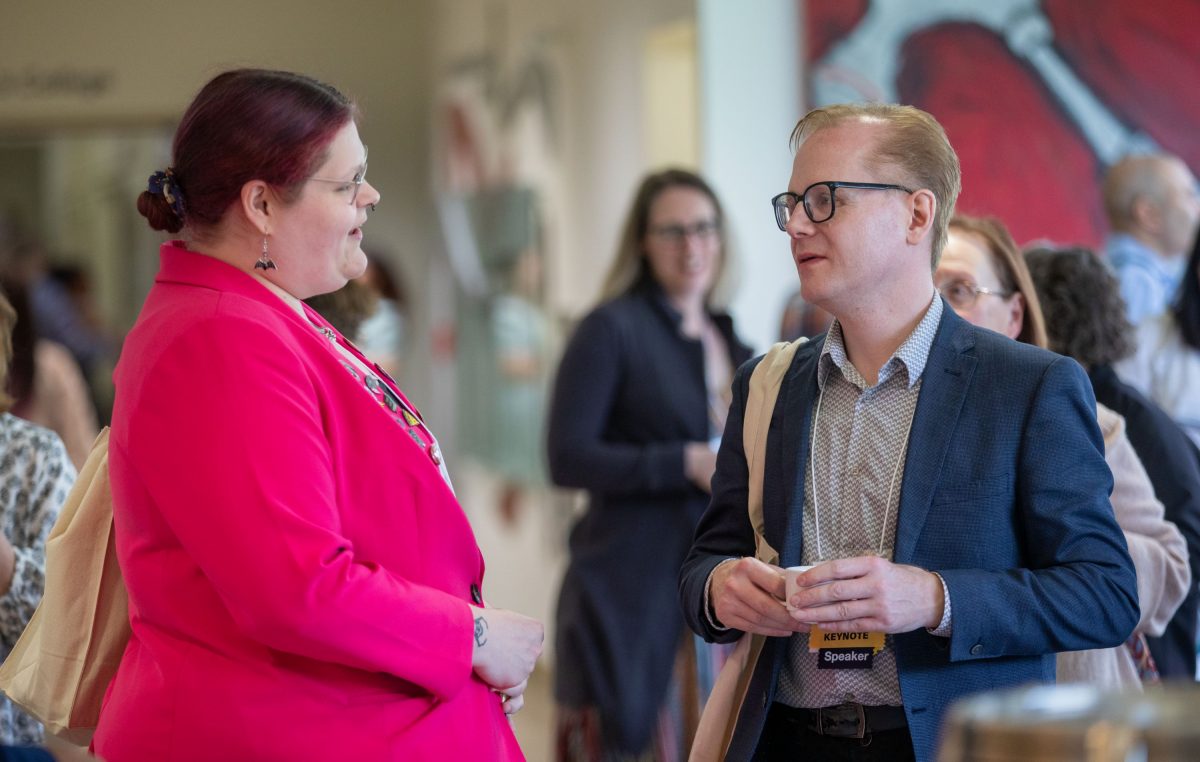 Two people having a conversation wearing business casual clothes in a colorful hallway.