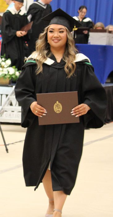 Lynette Trinidad, wearing a cap and gown at convocation, walks proudly with her new degree.