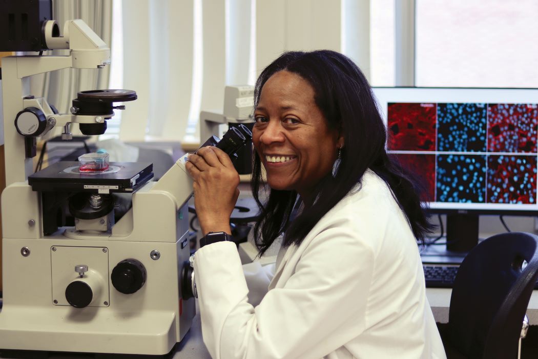 Dr. Yvonne Myal sits in front of a microscope in her lab.