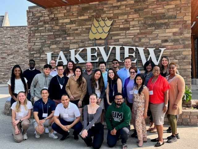 A big group of U M students standing in front of the Hecla Lakeview hotel sign in Manitoba.