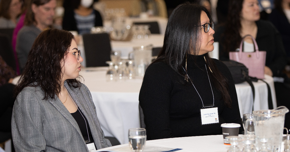 Two Indigenous women sitting at a conference, they are not looking at the camera.