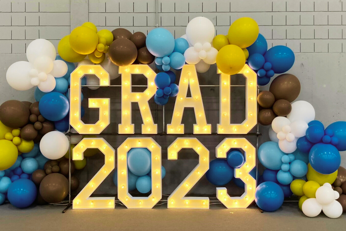 marquee letters spelling "grad 2023" surrounded by white, brown, gold and blue balloons
