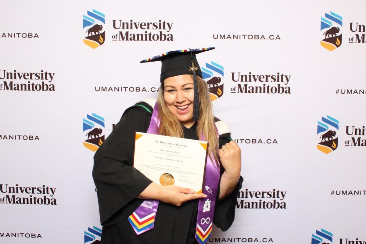 asper graduate stands in celebratory pose in graduation cap and gown with degree