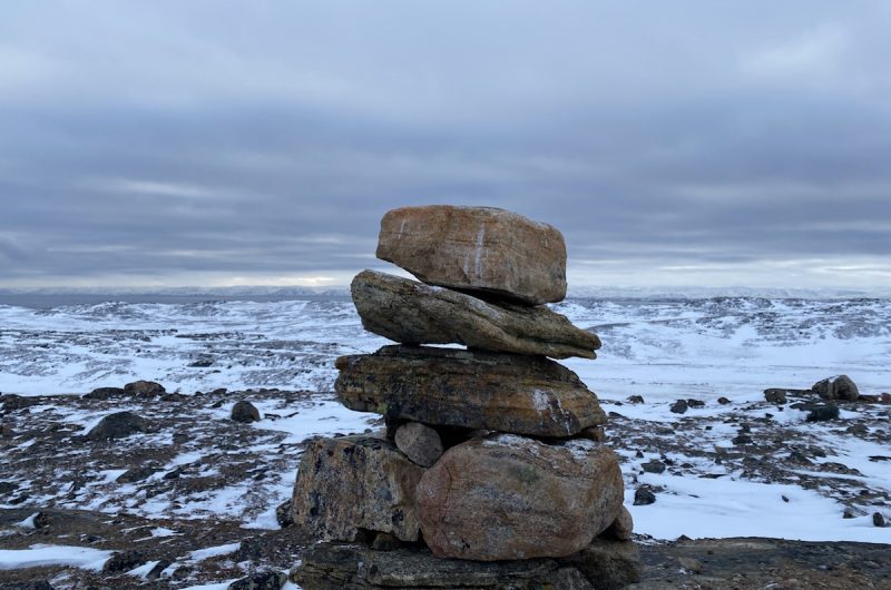 View of an Inukshuk with snowy, rocky landscape.