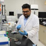 Md Mahamudul Haque wears a lab coat in a research lab. He inspects a petri dish.