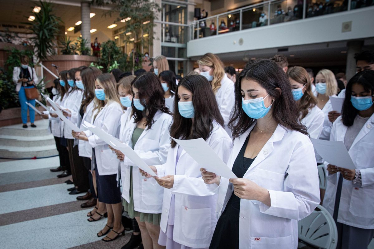 First-year medical students wearing white coats stand to read and recite the Physician's Pledge.