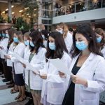 First-year medical students wearing white coats stand to read and recite the Physician's Pledge.