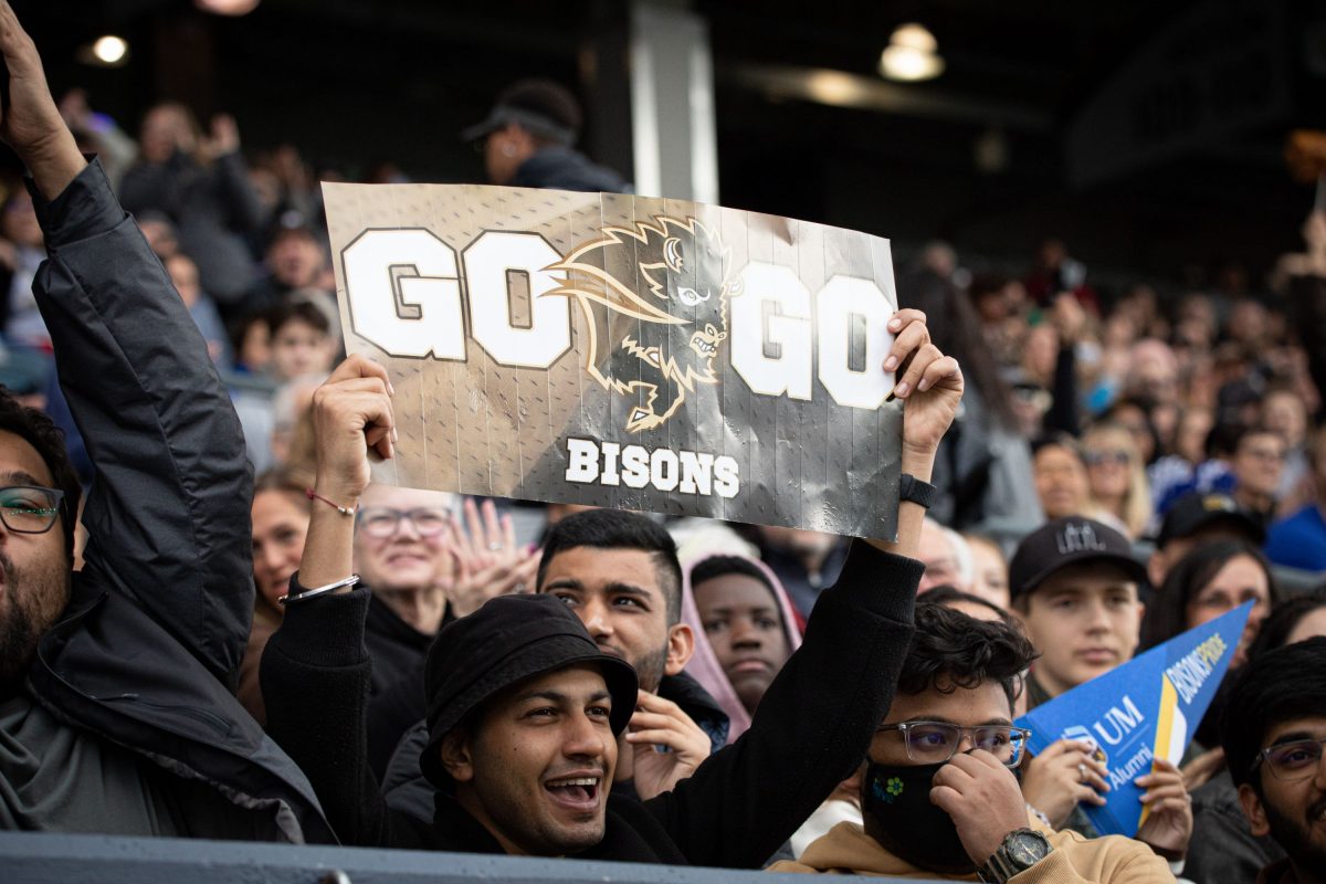 Group of fans cheering on the Bison football team and holding a sign that says 'Go Bisons'.