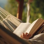 Person laying in a hammock, reading a book. Their face is not visible.