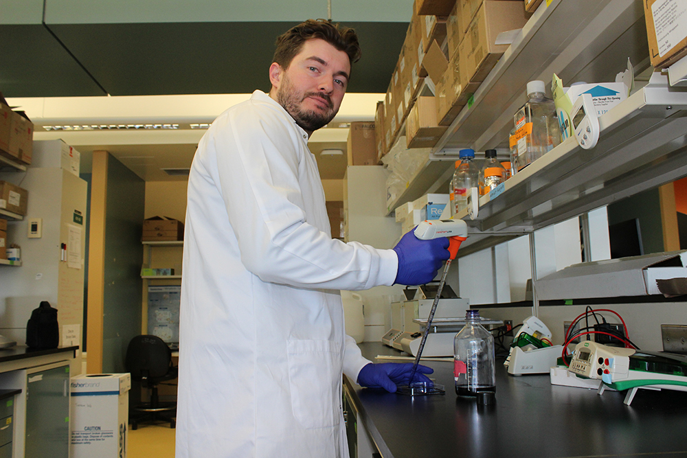 A male student wearing a white lab coat working in a laboratory.