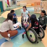 Three children in wheelchairs in a circle with two occupational therapy students.