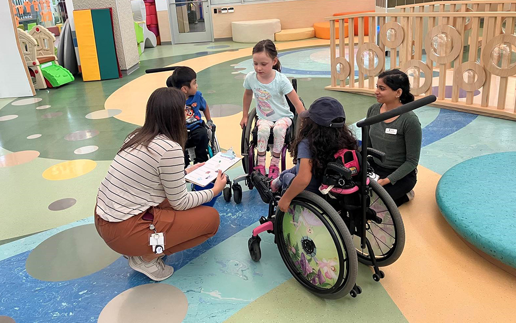 Three children in wheelchairs in a circle with two occupational therapy students.