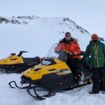 Two researchers standing next to their snowmobiles in snow.