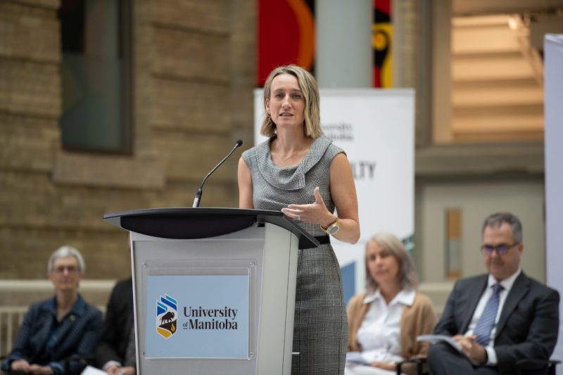 Dr. Joss Reimer speaks at a lectern. On the lectern are the words "University of Manitoba" and the UM logo. 