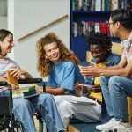 A diverse group of young people chatting in college library including female student with disability.