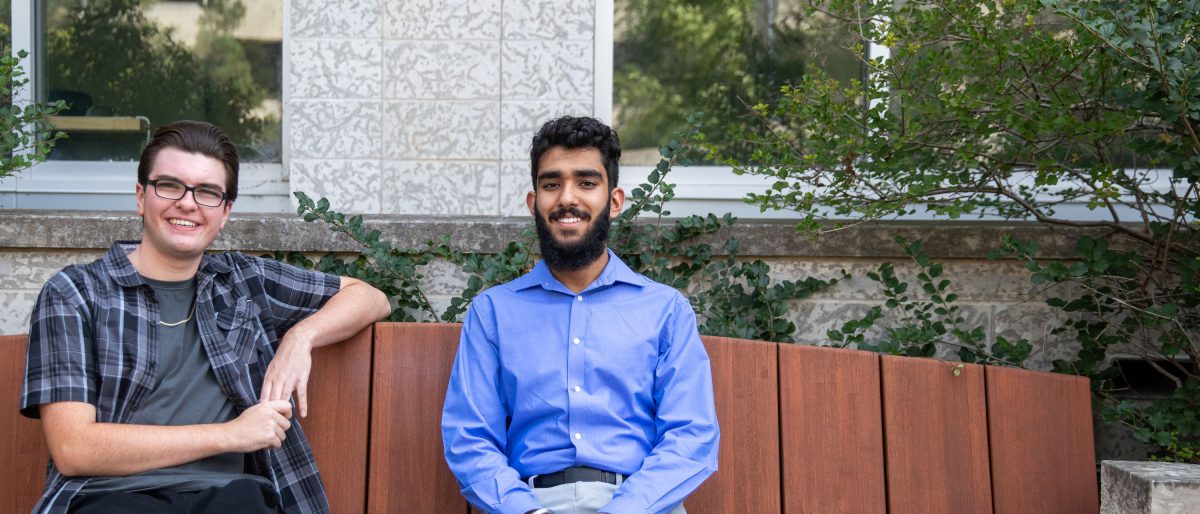 Schulich Leaders Cody and Simar sit on a brown bench outside UM's engineering building.