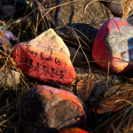 A pile of painted rocks stacked just inside the tall gates that separate the grounds of the former Qu'Appelle Industrial School and a railway line in the fall of 2021. The former school site sits on the western-most edge of the townsite. (Bryan Eneas/CBC)