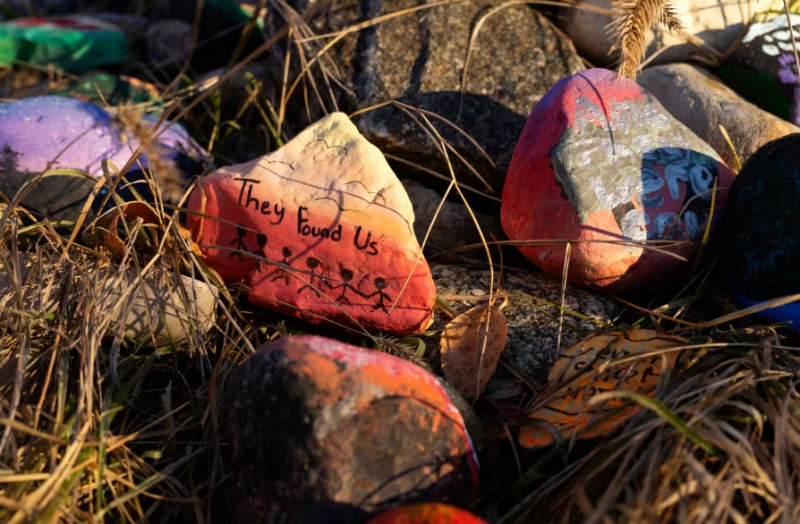 A pile of painted rocks stacked just inside the tall gates that separate the grounds of the former Qu'Appelle Industrial School and a railway line in the fall of 2021. The former school site sits on the western-most edge of the townsite. (Bryan Eneas/CBC)