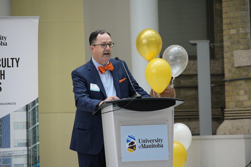 Dr. Peter Nickerson, dean of the Rady Faculty of Health Sciences, speaks at a podium in front of balloons at the Bannatyne campus.
